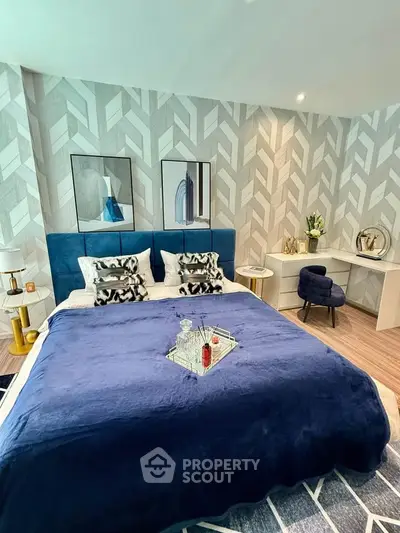 Luxurious bedroom with modern decor, featuring a plush blue bedspread and stylish geometric wallpaper.