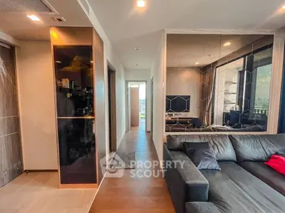 Modern living room with sleek design and large sofa, featuring a hallway leading to a bright balcony view.