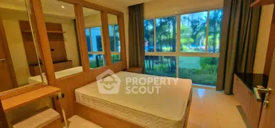 Spacious bedroom with large windows offering a lush garden view, featuring modern wooden furnishings and ample natural light.