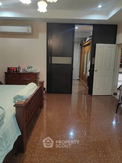 Spacious bedroom with wooden furniture and glossy flooring, featuring a sliding door to an adjacent room.