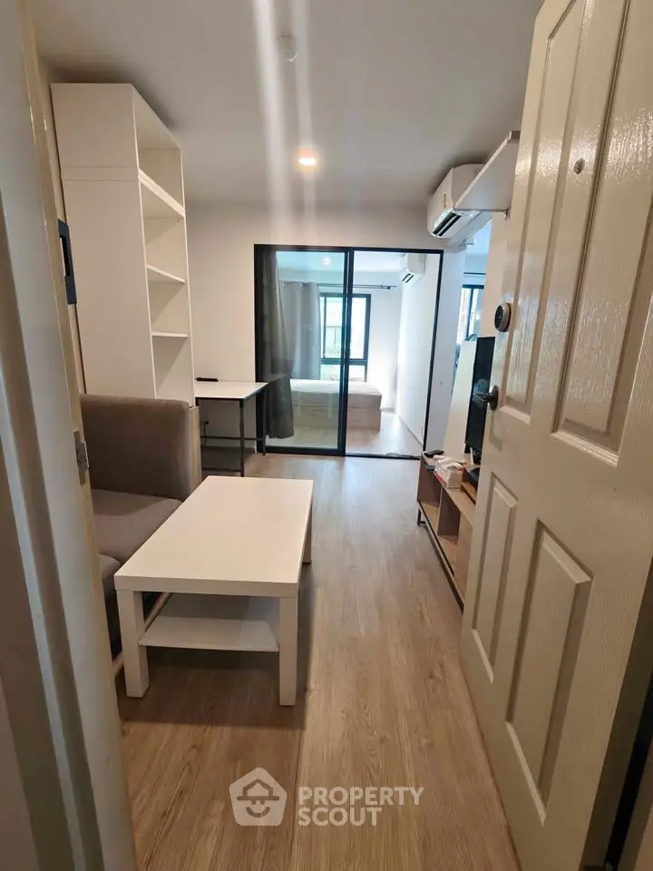 Modern apartment interior with open living room and bedroom, featuring sleek furniture and wooden flooring.