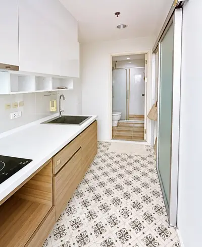 Modern kitchen with sleek cabinetry and patterned tile flooring leading to a bathroom.