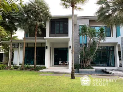 Modern two-story home with expansive glass windows, surrounded by lush greenery and palm trees, featuring a serene outdoor pool.