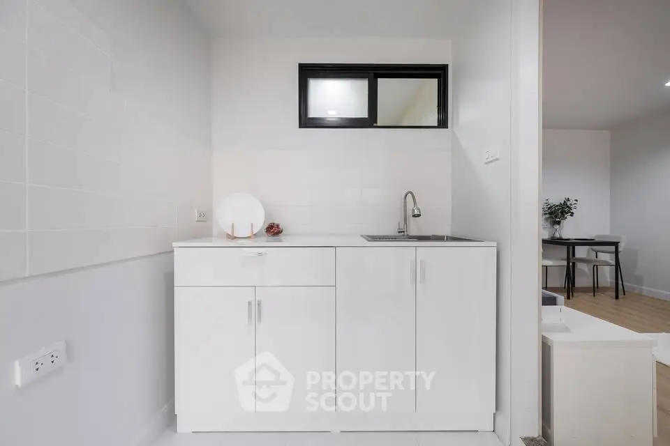 Modern minimalist kitchen with sleek white cabinetry and stainless steel sink, perfect for compact living spaces.