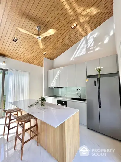 Modern kitchen with sleek design, high ceiling, and natural light featuring island and stainless steel appliances.