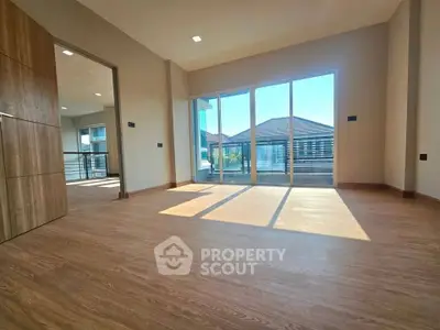 Spacious sunlit room with large windows and wooden flooring in modern home.