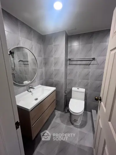 Modern bathroom with sleek gray tiles and round mirror, featuring a stylish vanity and toilet.