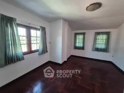 Spacious empty room with hardwood floors and large windows in a well-lit home.