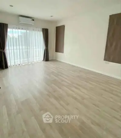 Spacious empty room with wooden flooring and large window
