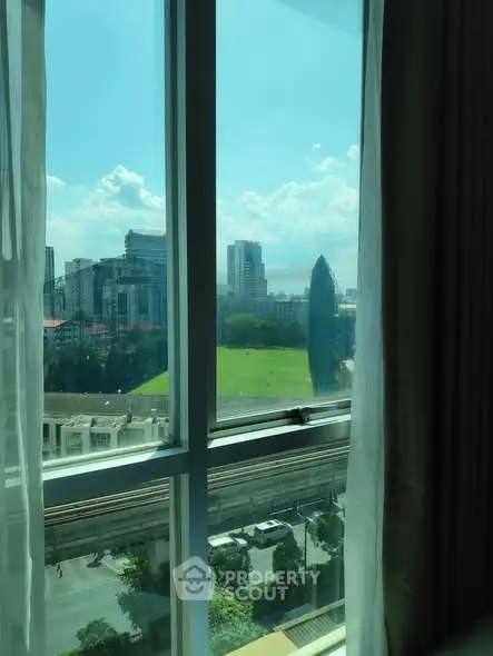 Stunning cityscape view from a high-rise apartment window, showcasing lush greenery and modern architecture.