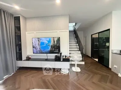 Modern living room with stylish decor and staircase, featuring a large TV and elegant flooring.