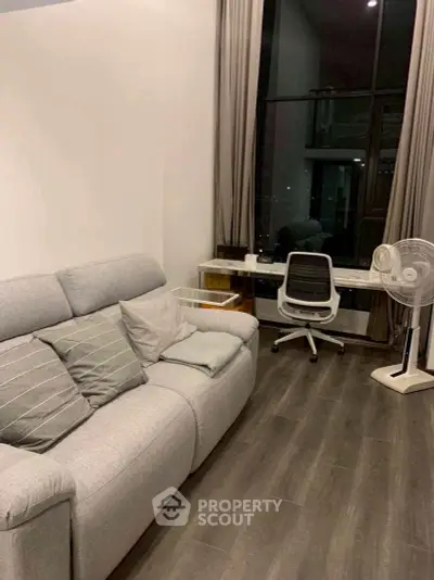 Modern living room with stylish sofa and workspace by large window.