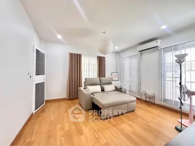 Spacious living room with modern furniture and wooden flooring, featuring large windows and ample natural light.