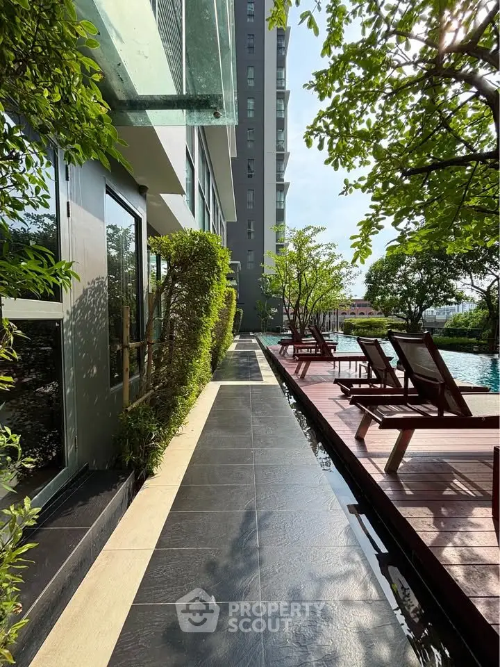 Luxurious poolside area with sun loungers and lush greenery in modern residential complex.