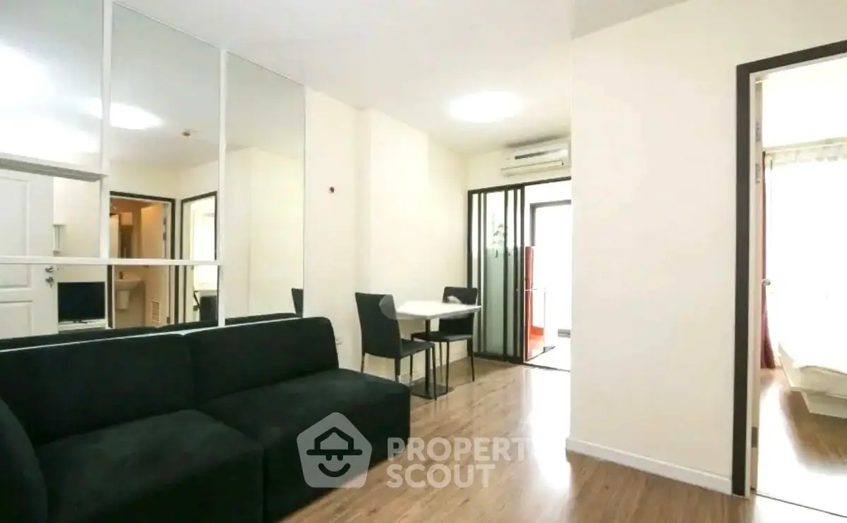 Modern living room with sleek black sofa and dining area in open layout apartment.
