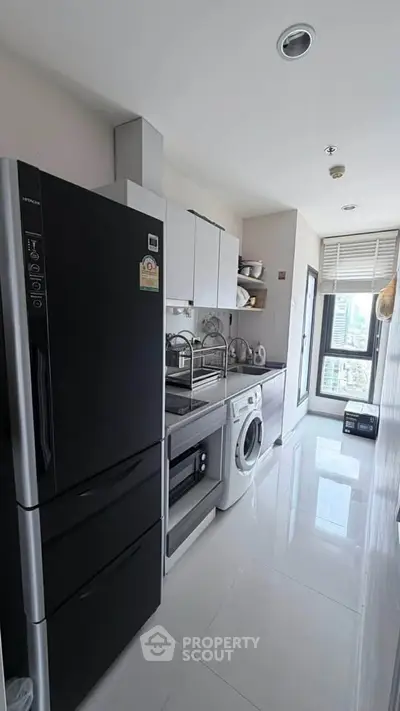 Modern kitchen with sleek appliances and city view, featuring a washing machine and refrigerator.