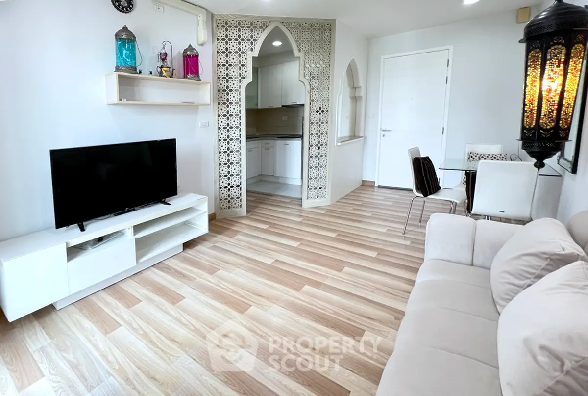 Charming living room with modern decor and open kitchen layout, featuring elegant lighting and wooden flooring.