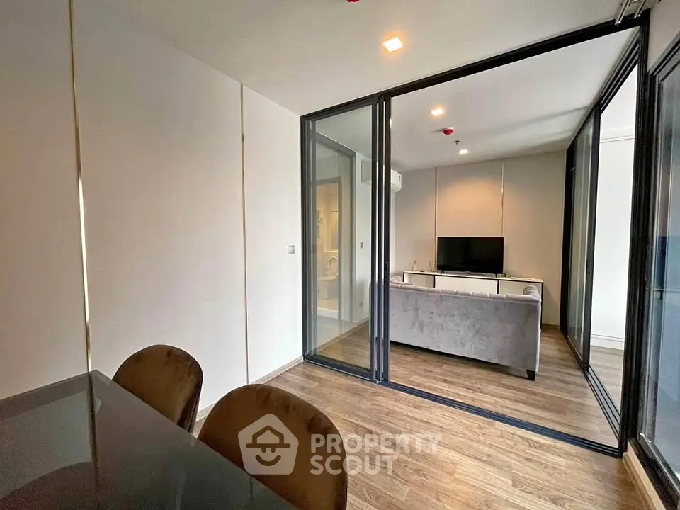 Modern living room with glass partition and wooden flooring, featuring a cozy sofa and TV setup.