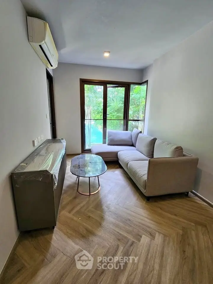 Modern living room with large windows and stylish furniture overlooking lush greenery.