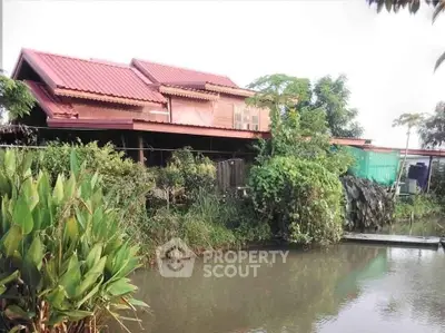 Charming riverside house with lush garden and red roof, perfect for nature lovers.