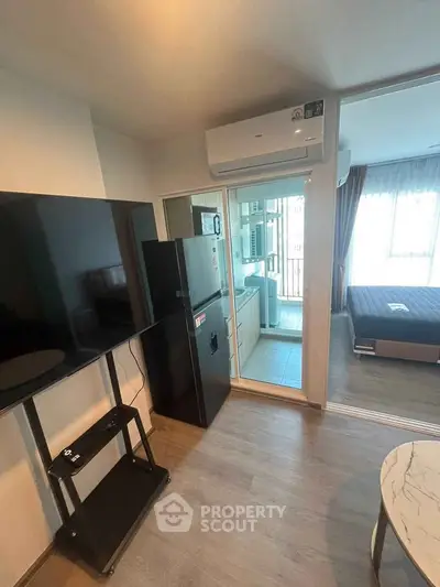 Modern apartment interior with sleek kitchen and cozy living area, featuring a large TV and air conditioning.
