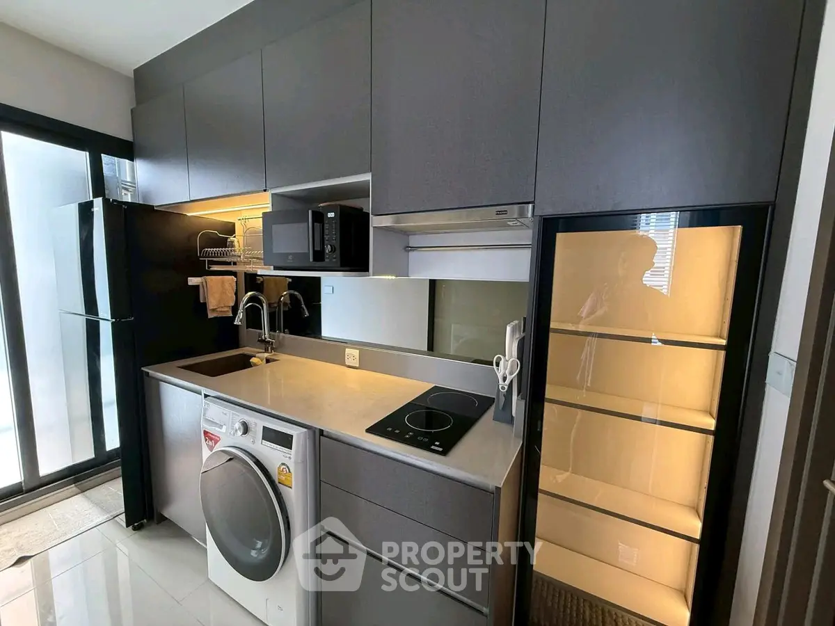 Modern kitchen with sleek cabinetry, washing machine, and induction cooktop in a stylish apartment.