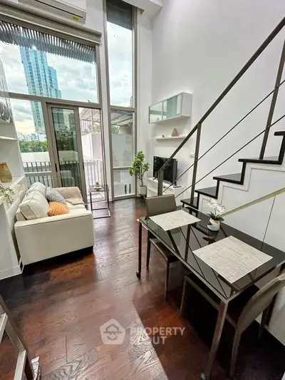 Modern duplex living room with high ceiling and city view, featuring sleek furniture and elegant decor.