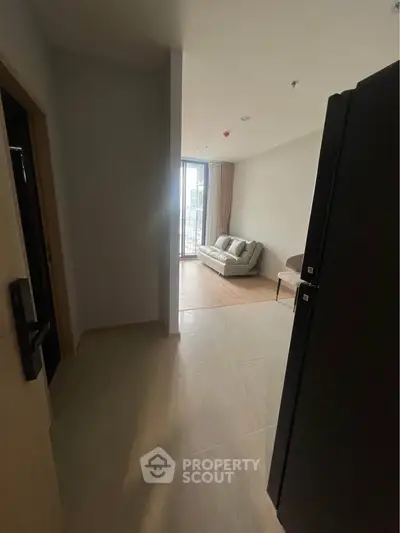 Modern apartment entrance leading to a cozy living room with a large window and stylish sofa.