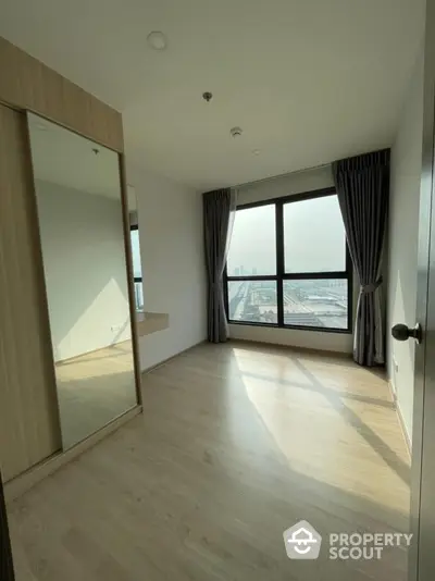 Spacious bedroom with large window offering stunning city view and ample natural light.