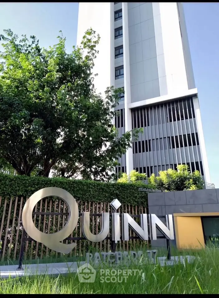 Modern high-rise building with lush greenery and prominent signage in urban setting.