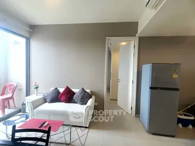 Modern living room with cozy sofa, glass coffee table, and sleek refrigerator in a bright apartment.