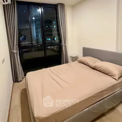 Cozy bedroom with large window and modern furnishings in urban apartment.