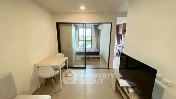 Modern apartment interior with open living room and bedroom view, featuring sleek furniture and natural light.