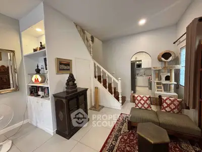 Charming living room with staircase and cozy decor, featuring a glimpse into a modern kitchen.