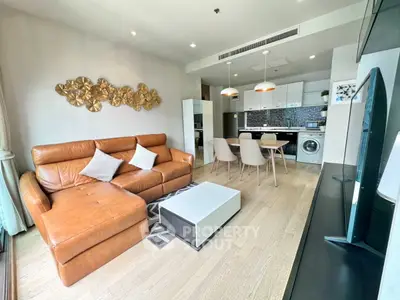 Modern living room with leather sofa and open kitchen featuring sleek appliances and stylish decor.