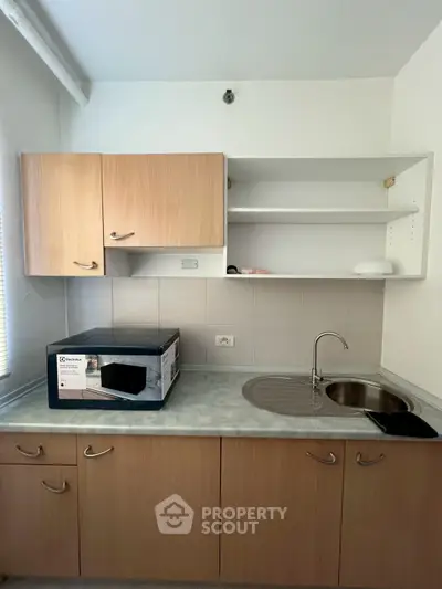 Compact kitchen with wooden cabinets and stainless steel sink, featuring a microwave on the counter.