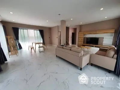 Spacious living room with elegant marble flooring, plush sofas, and a modern entertainment unit, leading to a sunlit balcony.