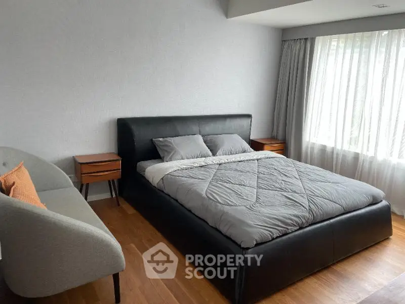 Modern bedroom with sleek black bed, wooden floor, and large window with natural light.