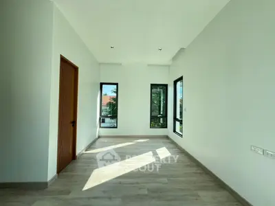 Spacious sunlit room with large windows and wooden door, perfect for modern living.