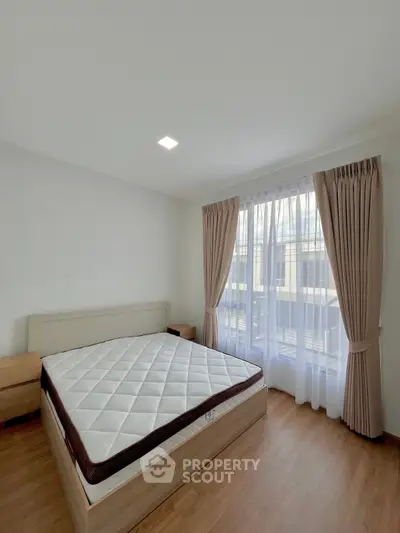 Spacious bedroom with large window and elegant curtains in modern apartment.