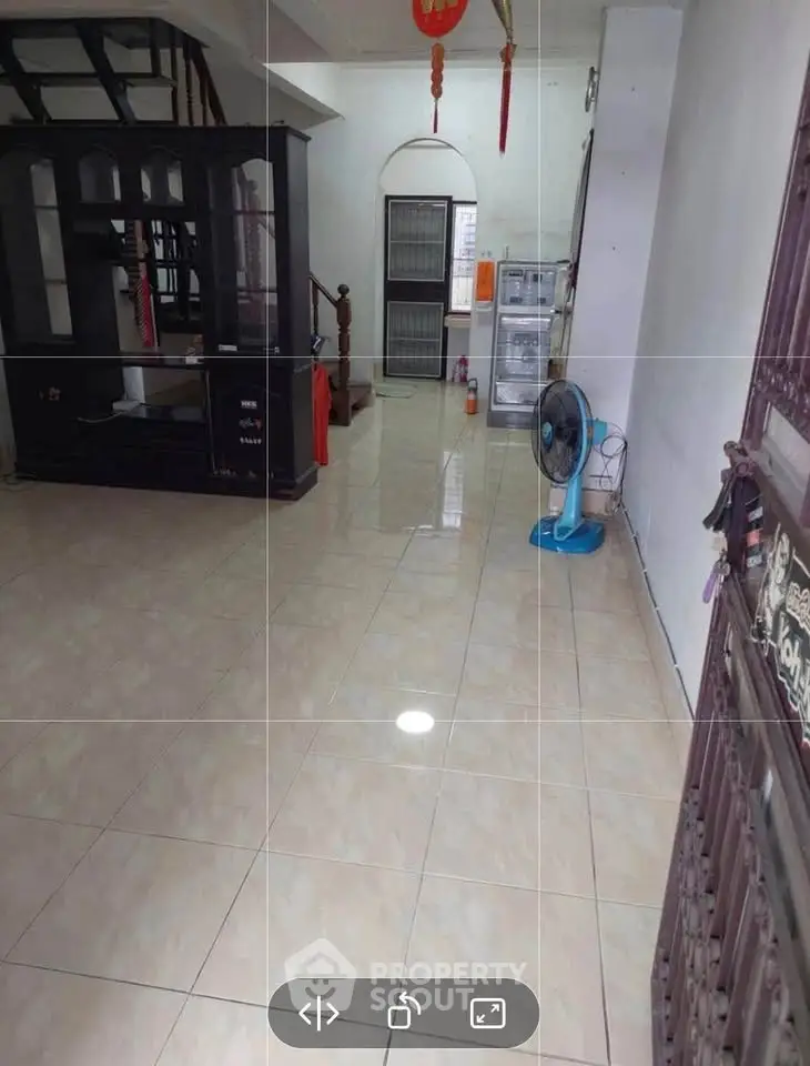 Spacious living area with tiled flooring and traditional decor, featuring a staircase and fan.