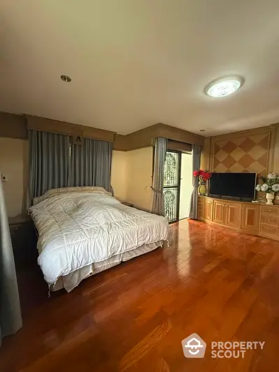 Spacious bedroom with elegant wooden flooring and large TV unit