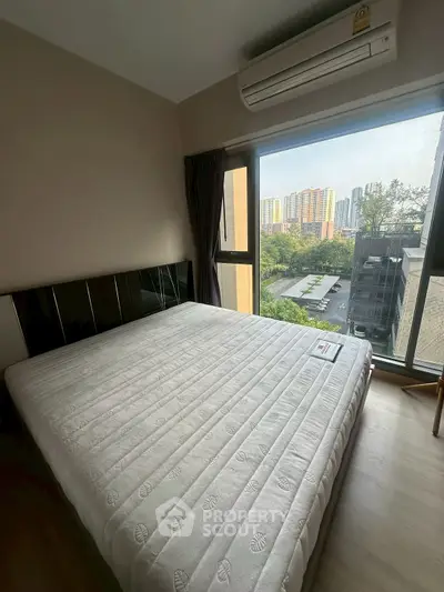 Spacious bedroom with large window offering stunning city view and natural light.