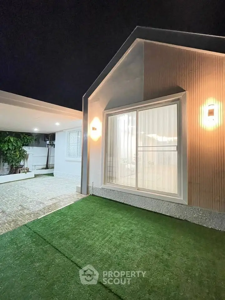Modern exterior view of a stylish home with well-lit facade and artificial grass lawn.