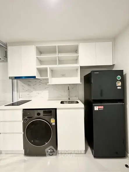 Modern kitchen with sleek white cabinetry, black fridge, and built-in washing machine.