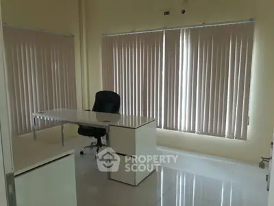 Modern office space with sleek desk and chair, featuring large windows and vertical blinds.