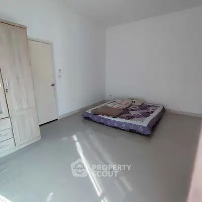 Minimalist bedroom with floor mattress and wardrobe, bright and spacious.