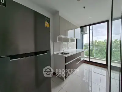 Modern kitchen with sleek cabinets and large fridge, overlooking a lush green view from the balcony.