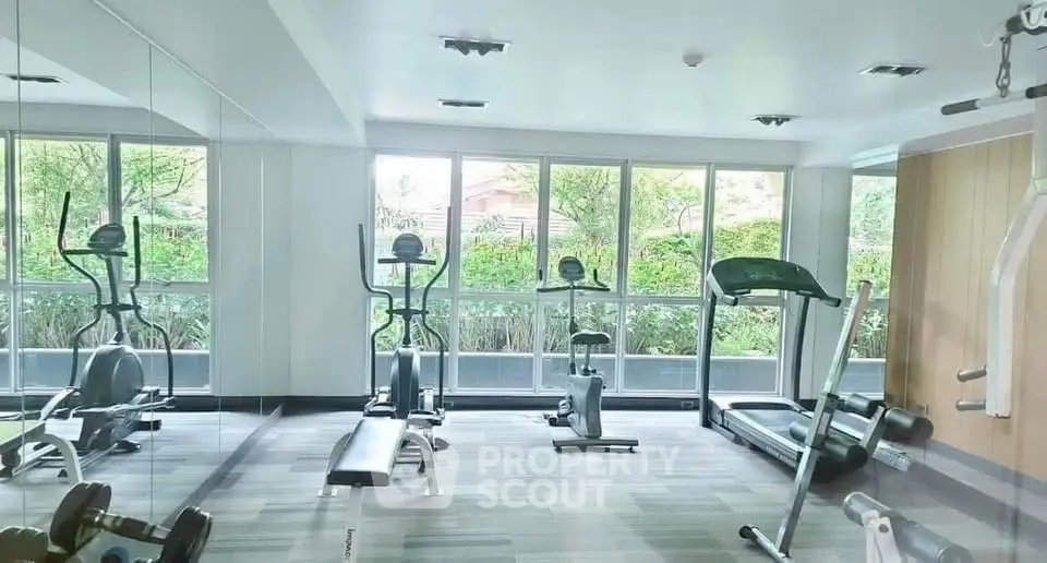 Spacious gym with modern equipment and large windows offering garden views.