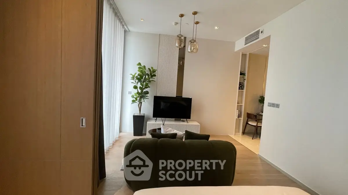 Modern living room with stylish decor and natural light, featuring a cozy sofa and flat-screen TV.